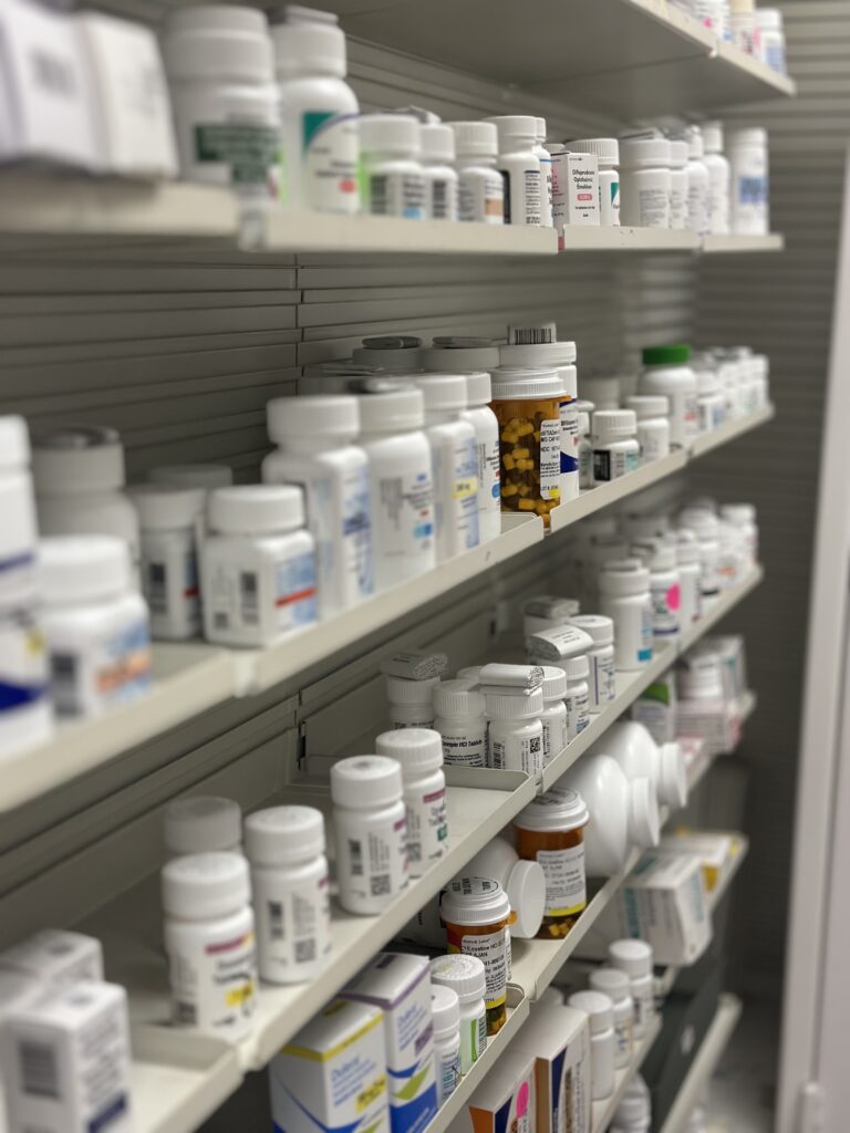 Pharmacy shelves stocked with prescription medication bottles and containers.